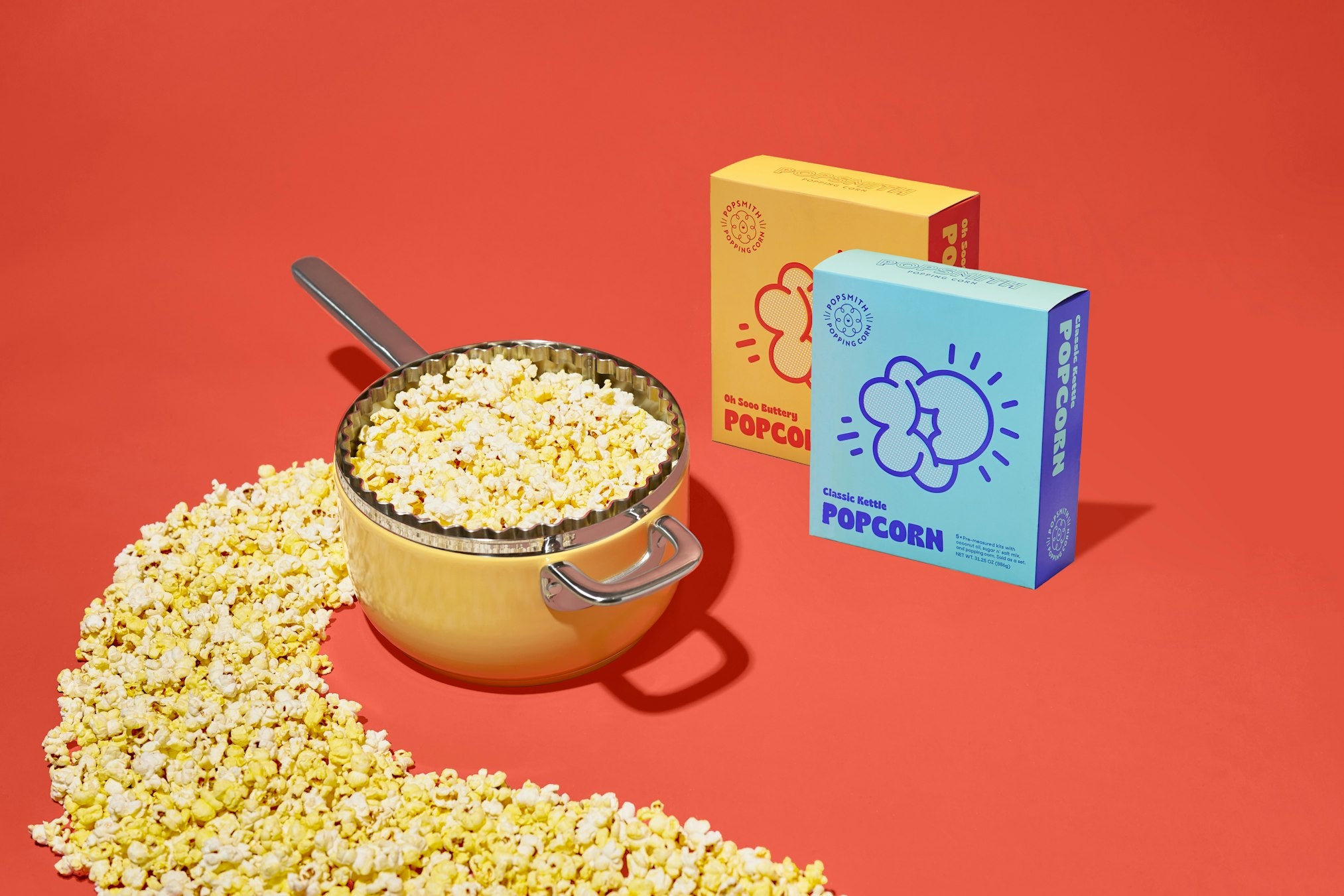 yellow popcorn popper next to two boxes of Popsmith popcorn on a red background
