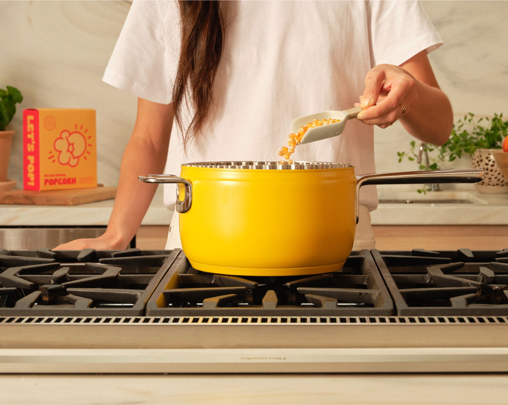 A woman adding popcorn kernels to a Popsmith popper on a stovetop.