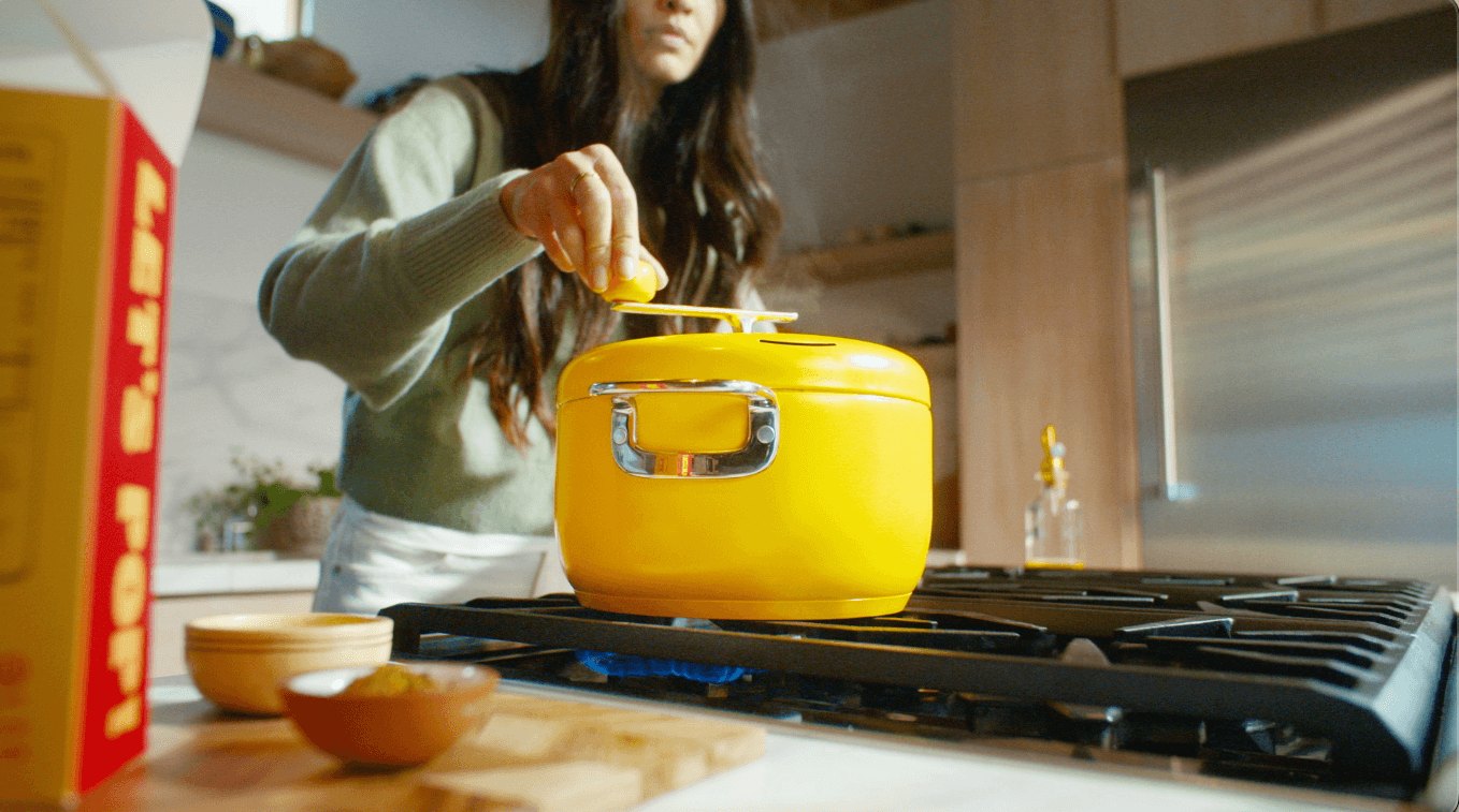 A hand turning the stirring handle on a yellow Popsmith popper on a gas stove