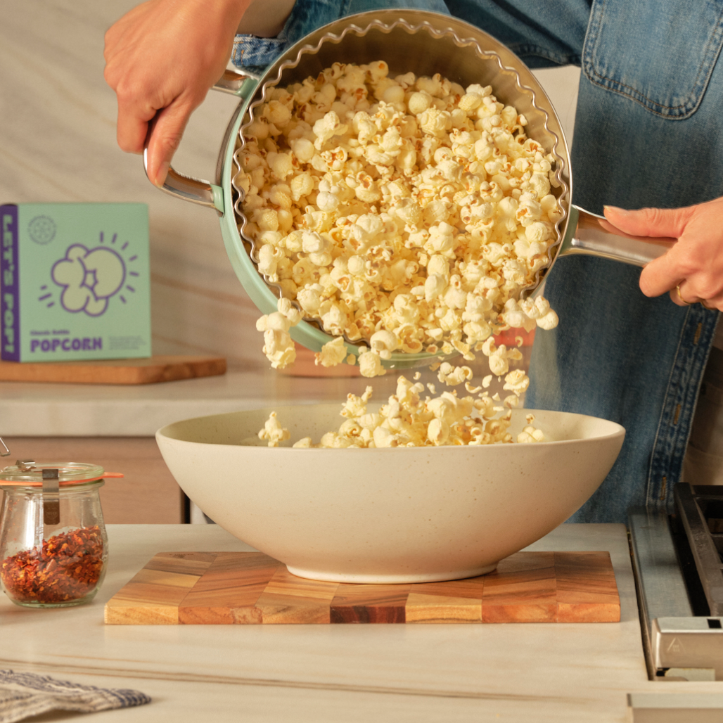 A woman pours fresh Kettle Corn Popcorn into a white bowl from a mint stovetop popcorn maker. [42751631360193]