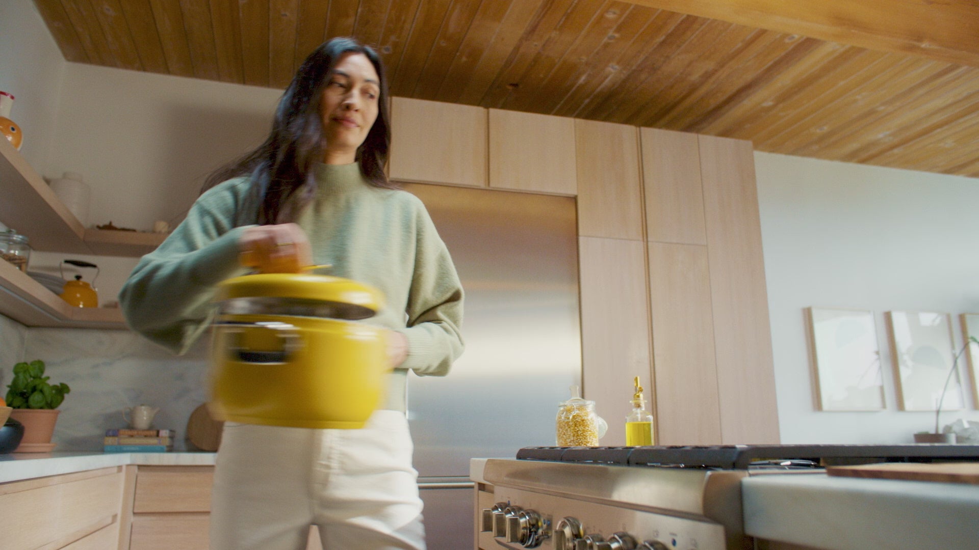 A woman in a bright kitchen carrying a Popsmith popper to the stove.