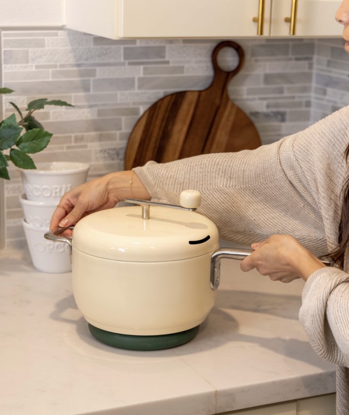 Hands lifting the lid off a cream Popsmith popper on the stove